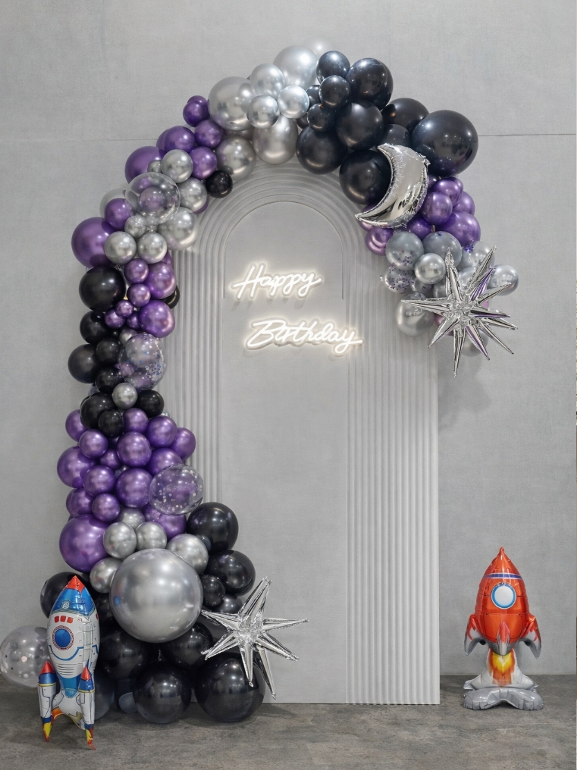 Outer space themed birthday party balloon garland with rocket, moon, and star balloons in purple, silver, and black.